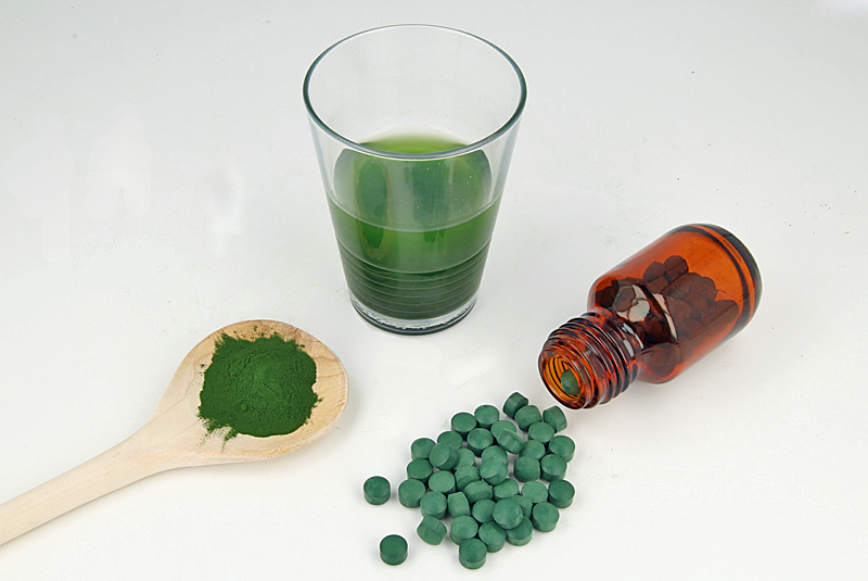 Zu sehen sind grüne Tabletten, grünes Pulver und eine trübe grüne Flüssigkeit im Glas